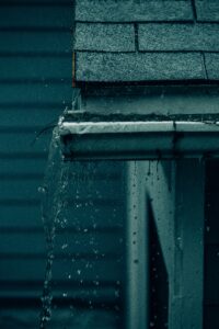 Rainwater overflowing from a clogged house gutter onto clean asphalt roof shingles.